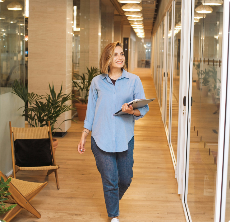 Businesswoman walking in a modern office with a tablet, representing streamlined workforce management and HR solutions for distributed teams.